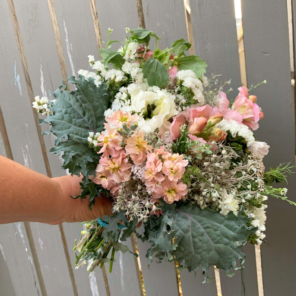 A close up of a bouquet of dusty rose, white, and sage green flowers.