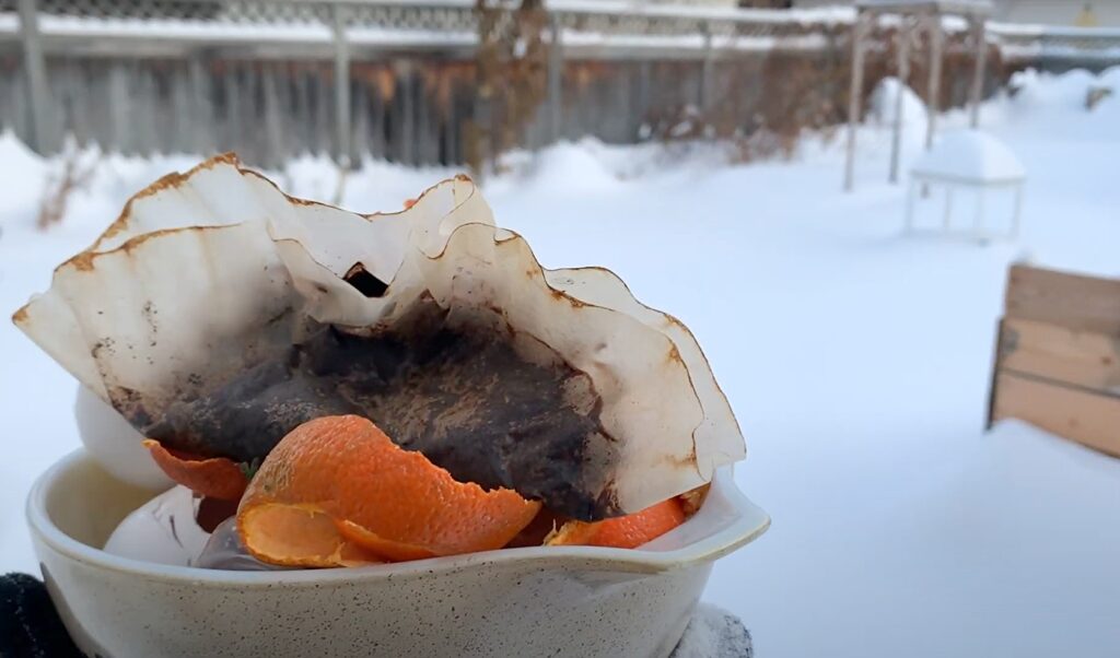 Coffee grounds and orange peel in a bowl with snow in the background.
