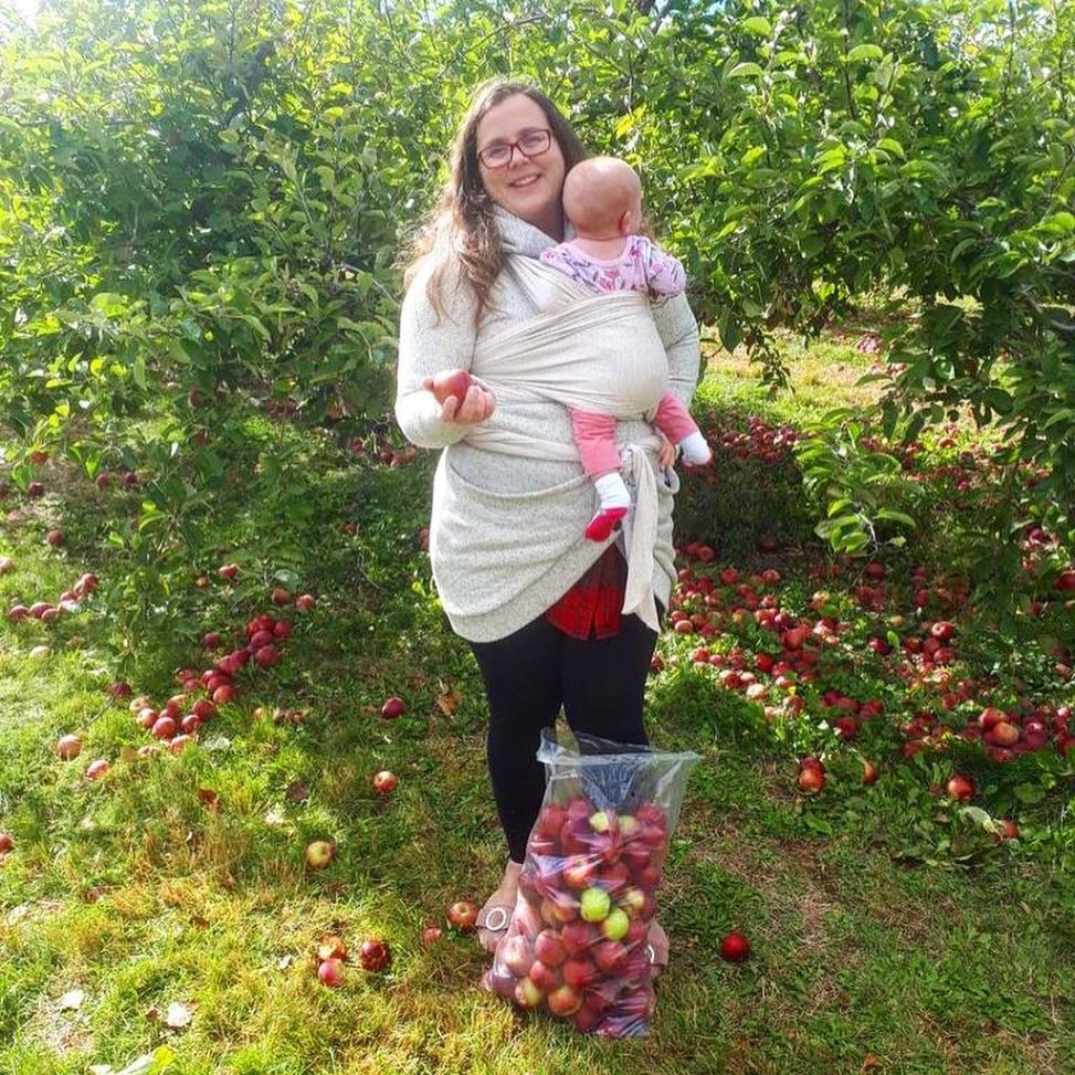 woman with baby in front of greenery with apples all around